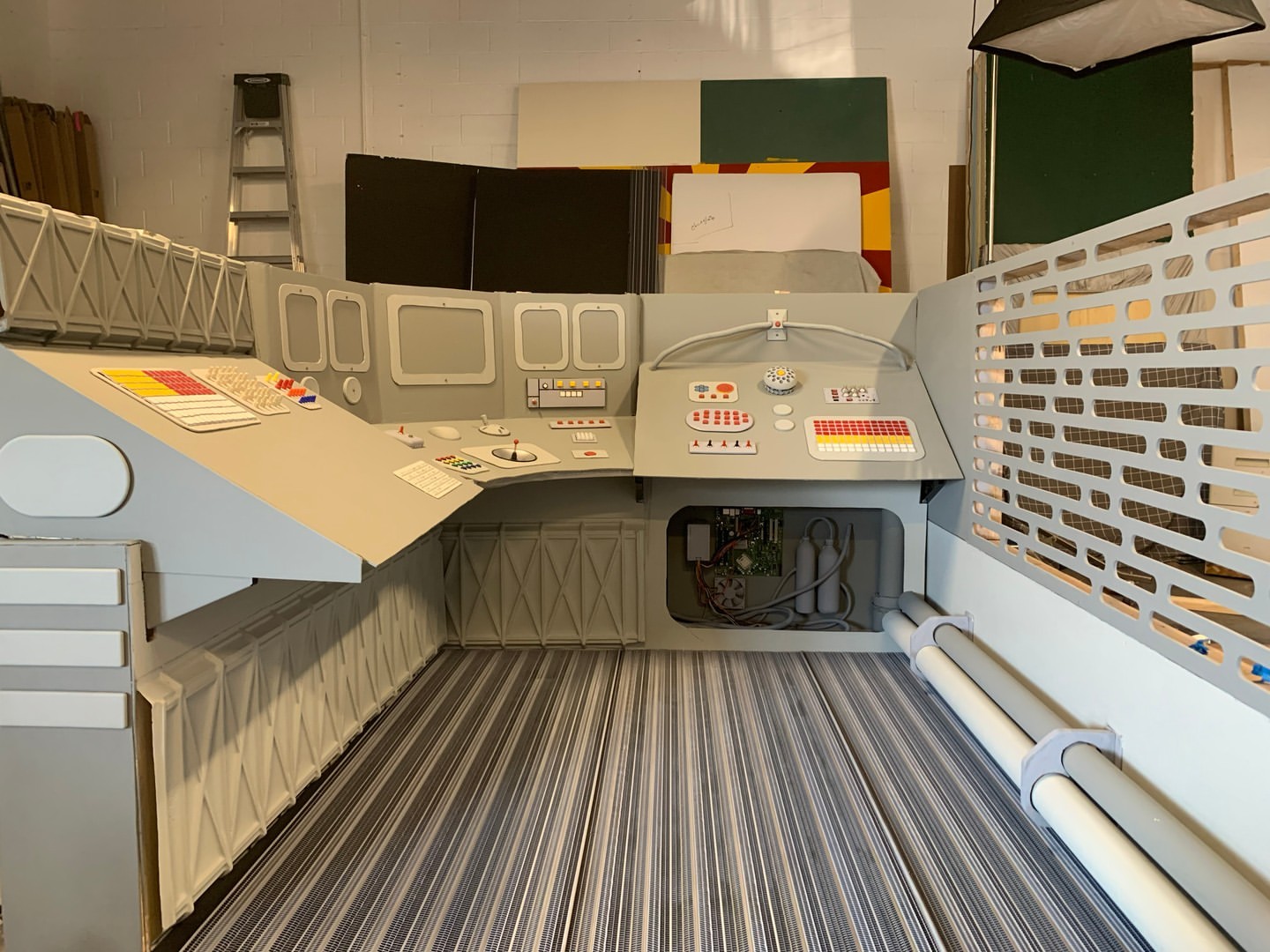 Intricate, gray spaceship interior set with panels of colorful buttons and a striped floor, evoking a high-tech, futuristic environment.